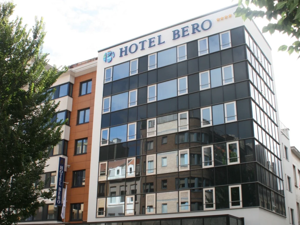 Glass-fronted facade of Hotel Bero with the hotel name in large letters along the roofline, framed by trees