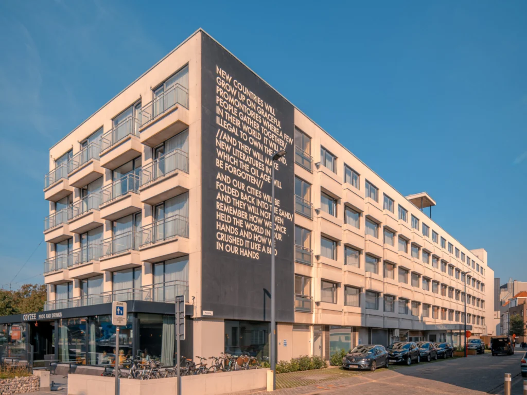 Modern five-storey Hotel Royal Astrid with balconies and a large poem on its dark corner wall, under a blue sky
