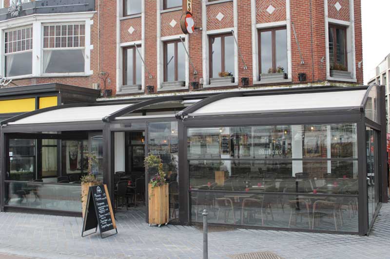 Red-brick facade of Hotel Rubens with a glazed, awning-covered brasserie terrace at street level