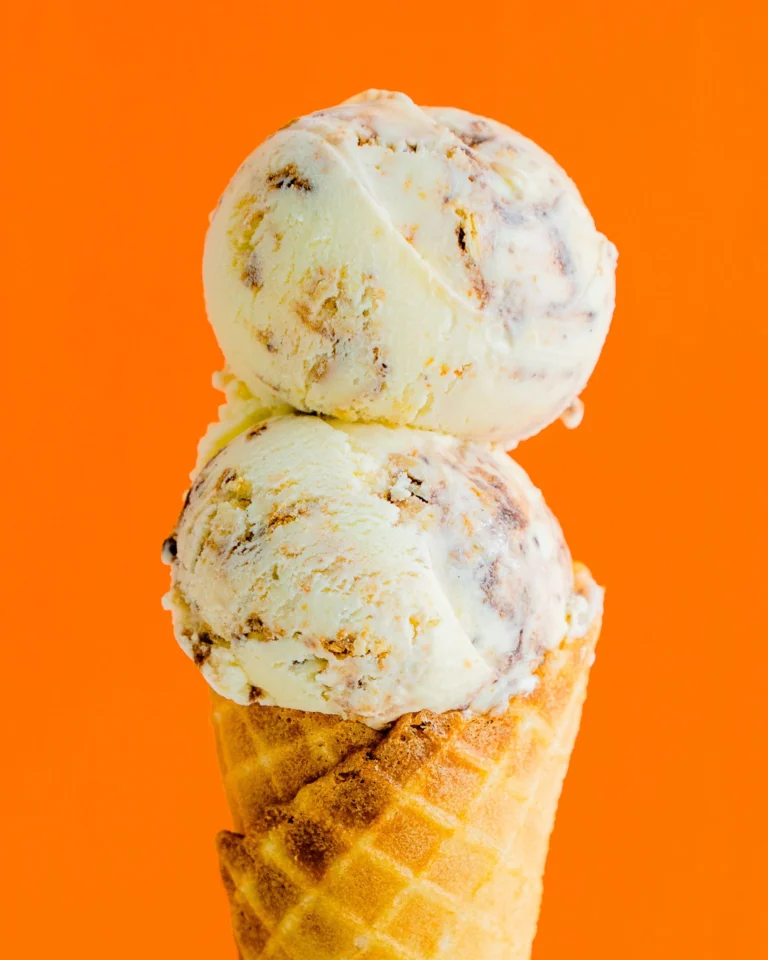 A double scoop of ice cream on a waffle cone against a bright orange background