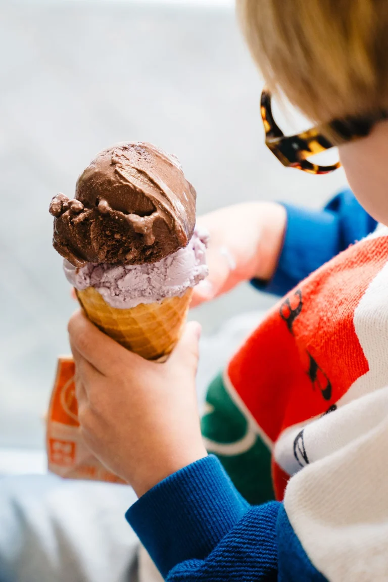 A hand holding a waffle cone with a scoop of chocolate ice cream on top of a purple scoop
