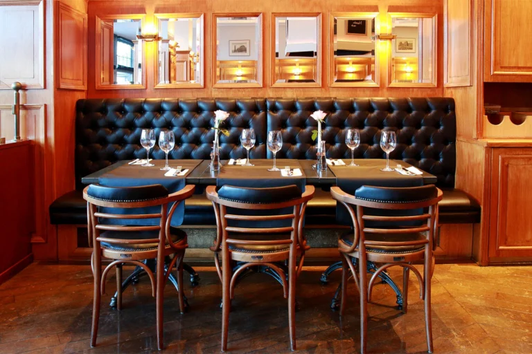 Laid tables in front of a buttoned black leather banquette beneath wood panelling and mirrors