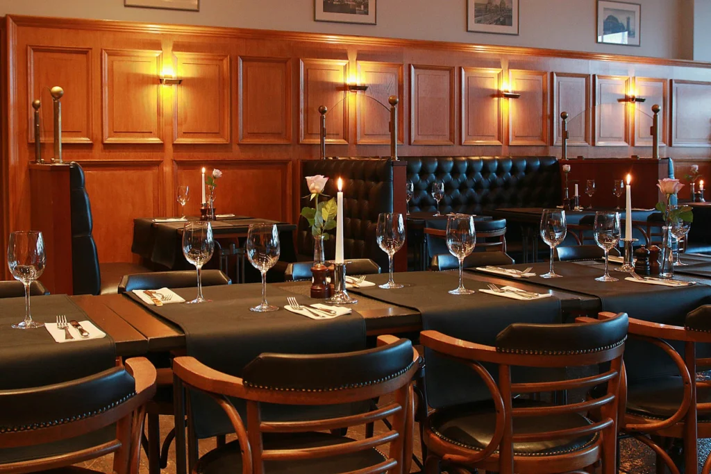 Wood-panelled dining room with dark tables, wine glasses, candles and black leather banquettes
