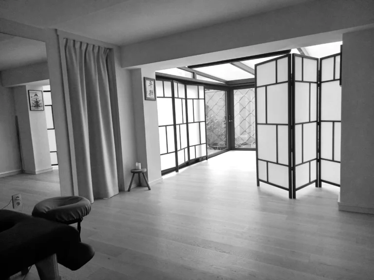 Black-and-white photo of an empty dojo with a wooden floor, shoji screens and a glass veranda