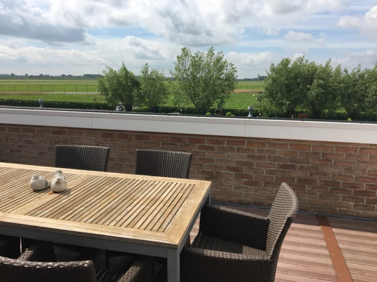 Terrace table and wicker chairs looking out over flat green polder fields and trees