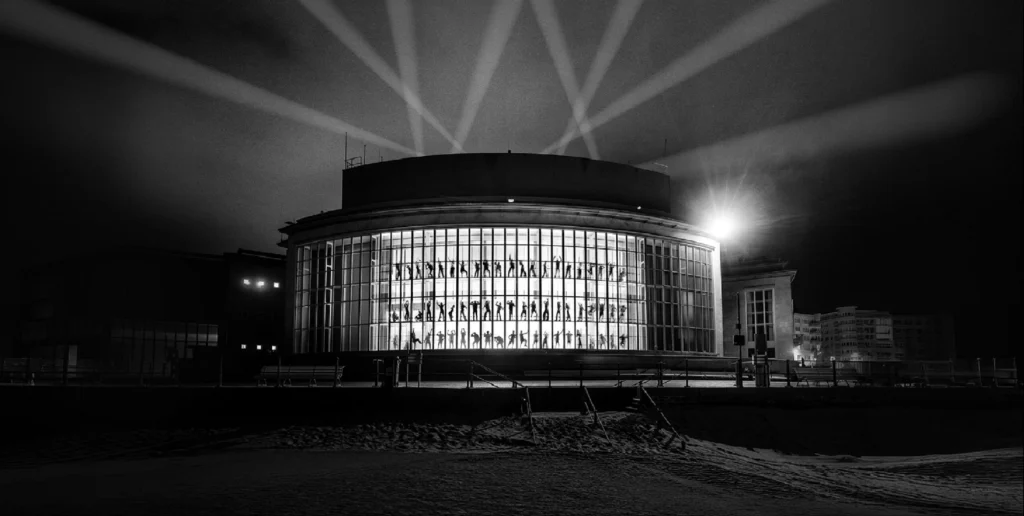 Black-and-white night view of the round, glass-fronted Kursaal on the beach with searchlights fanning into the sky