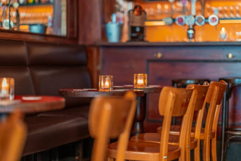 Wooden bar chairs and small tables with candles along a leather banquette in a warmly lit café