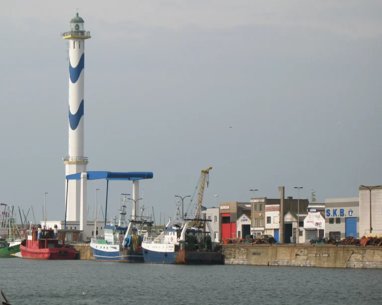 The lighthouse rising above the fishing dock, with red and white fishing boats moored at the quay