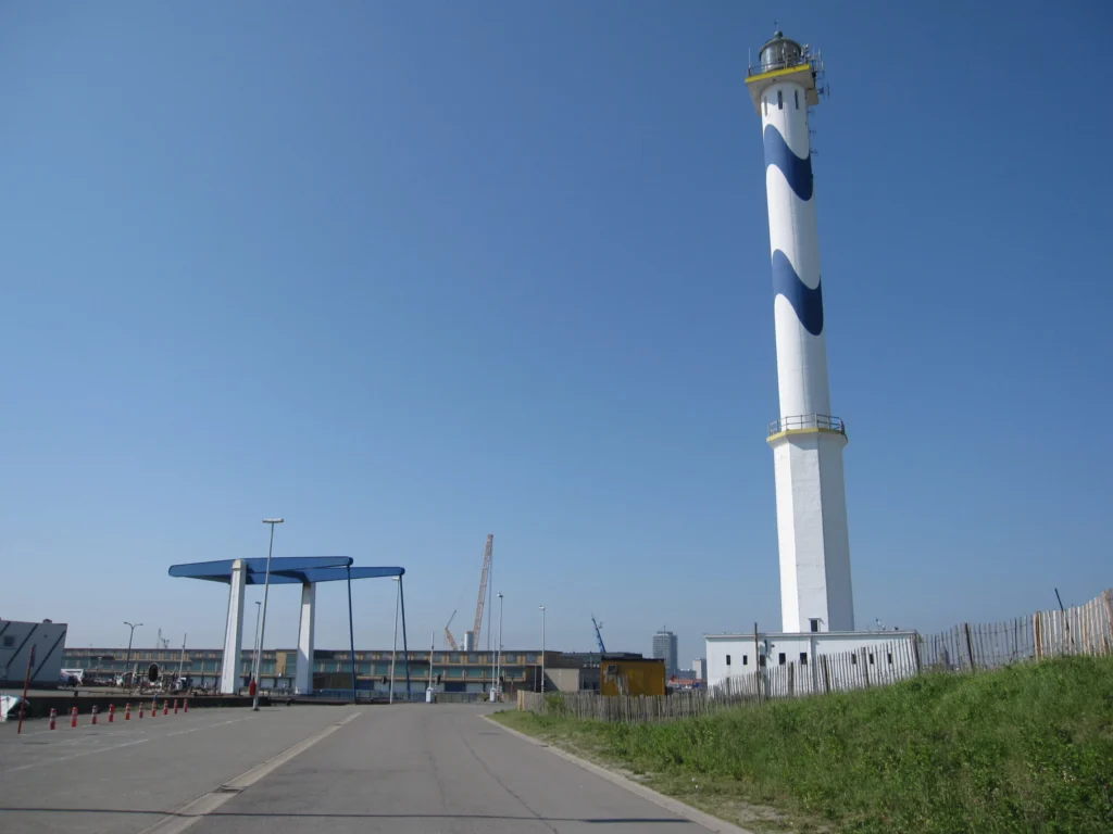 Tall white lighthouse with a blue wave pattern against a clear blue sky, a blue lift bridge frame beside it
