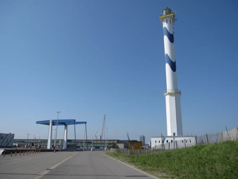 Tall white lighthouse with a blue wave pattern against a clear blue sky, a blue lift bridge frame beside it