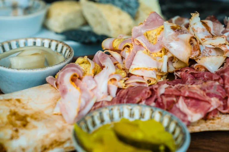 Board of thinly sliced cured meats with small bowls of pickles and bread