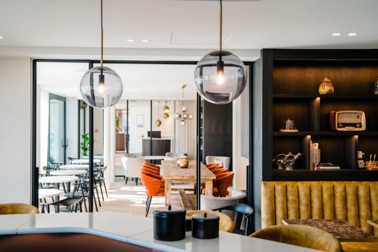 Bright lounge area with glass globe pendants, an ochre velvet banquette and dark display shelves