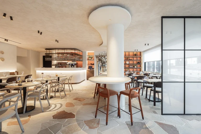 Brasserie interior with a marble-fronted bar, round tables, grey chairs and a crazy-paving stone floor