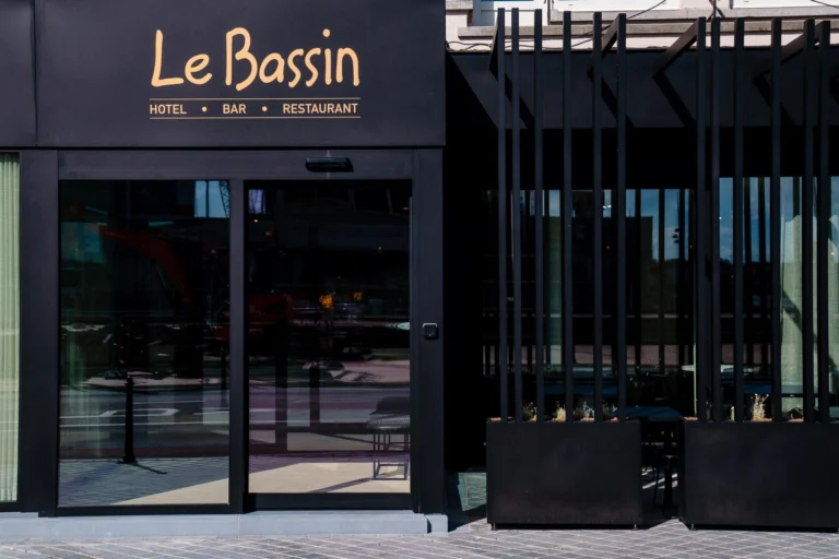 Black facade with gold Le Bassin hotel, bar and restaurant lettering above glass sliding doors