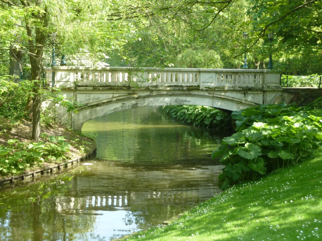 White balustraded bridge over the pond in Leopold Park, framed by trees and leafy banks