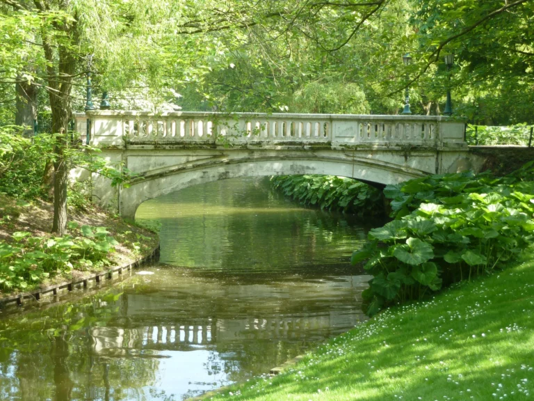 White balustraded bridge over the pond in Leopold Park, framed by trees and leafy banks
