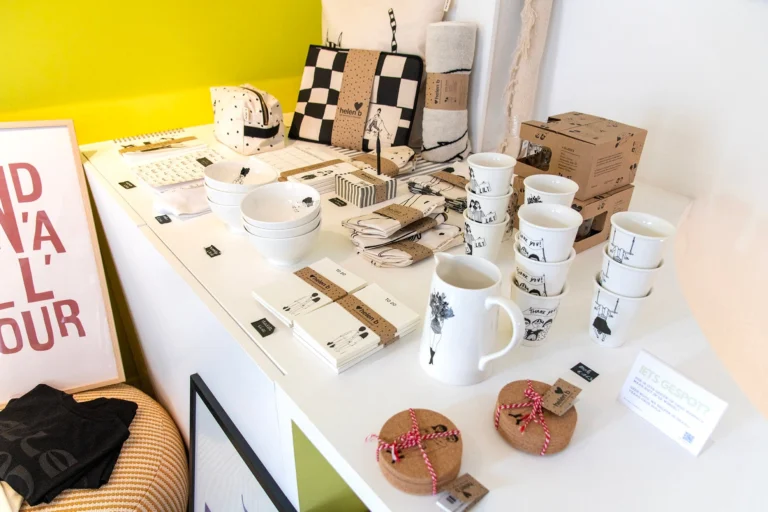 White display table with mugs, bowls, napkins and boxed gifts beside a framed red-lettered poster