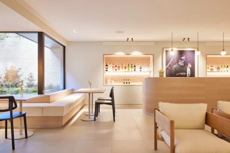 Light hotel lobby with a curved wooden counter, bar shelves, high tables and a patio window