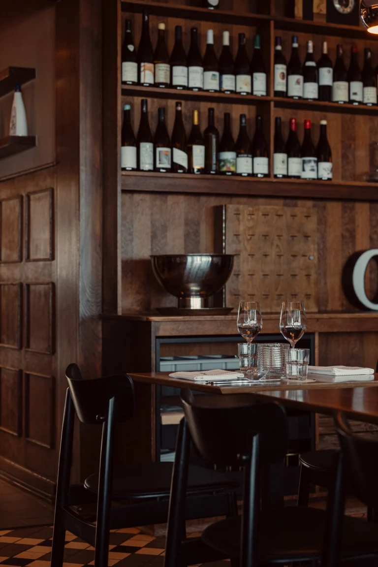 Dark wood-panelled dining room with a wall of wine bottles on shelves and a table set with wine glasses