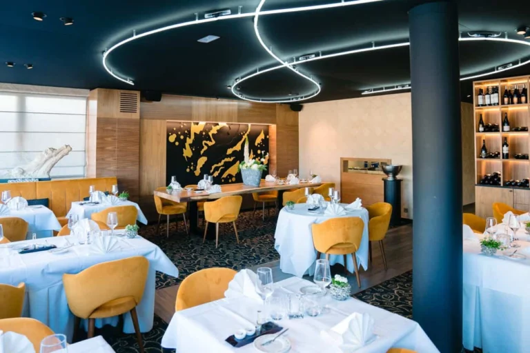 Dining room with white tablecloths, ochre velvet chairs, curved ceiling lights and a black-and-gold mural