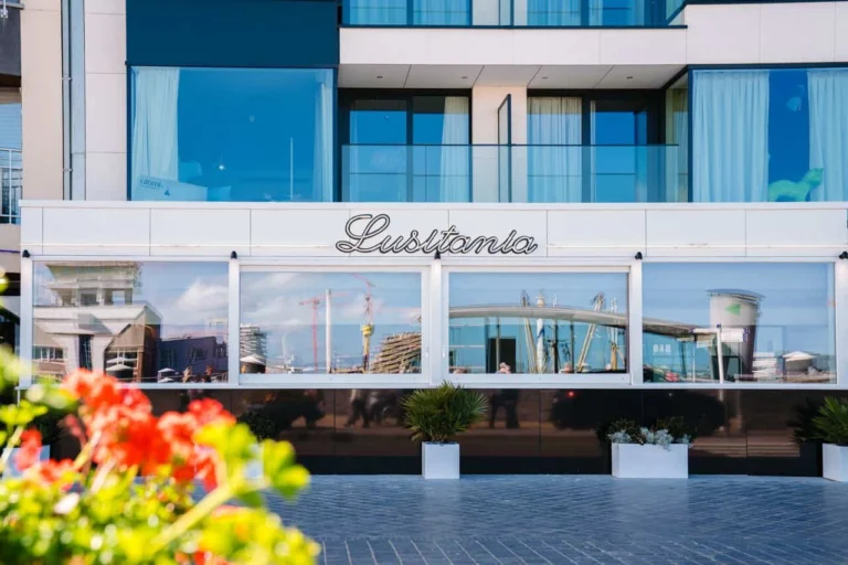 Lusitania's glass frontage with its script sign, red geraniums blurred in the foreground