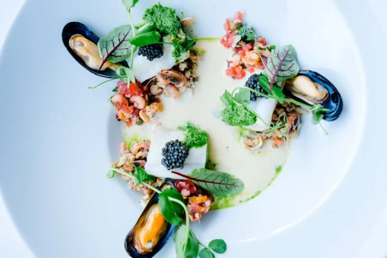 Mussels in their shells with caviar, diced tomato and herbs in a pale sauce on a white plate