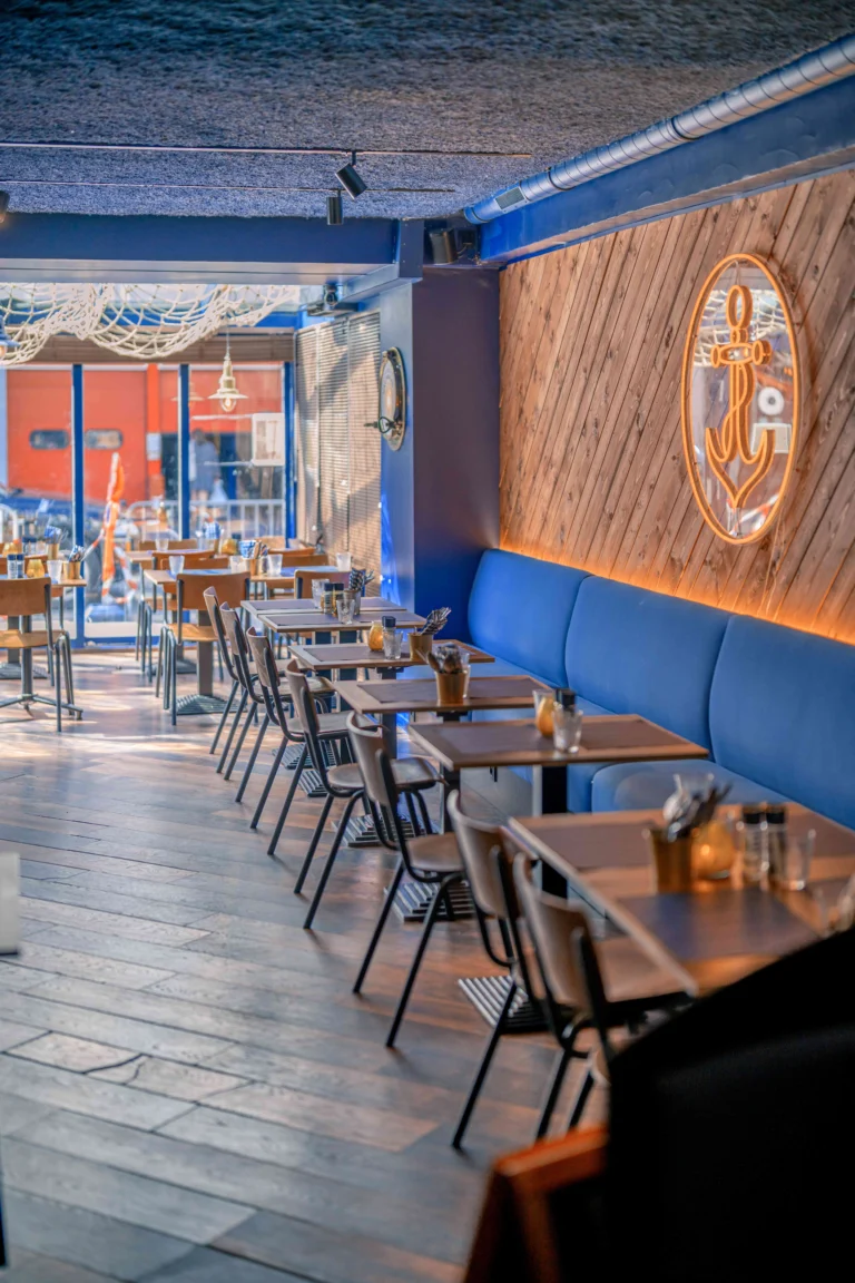 Looking along the dining room at Mac Moules towards the windows, with rows of wooden tables and the blue banquette and anchor sign on the right