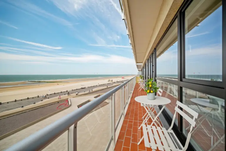 Long terracotta-tiled balcony with a white bistro table and chairs overlooking the beach and the North Sea