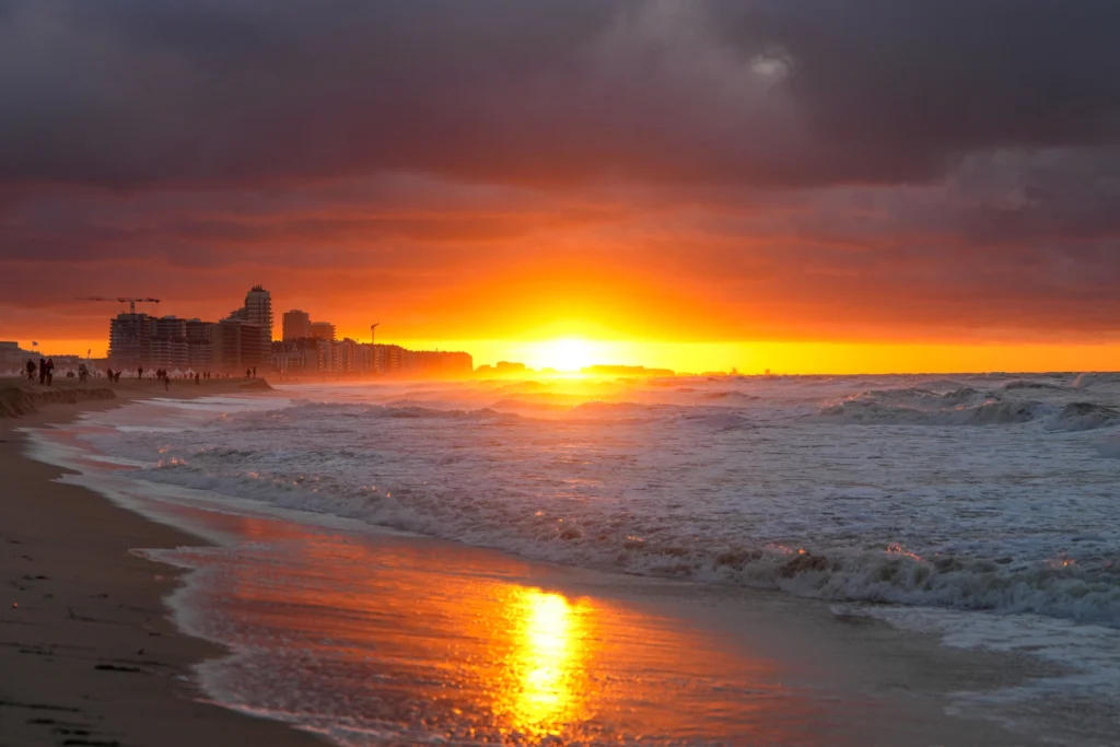 The sun setting over breaking waves on Mariakerke beach in Ostend, with apartment blocks along the shore