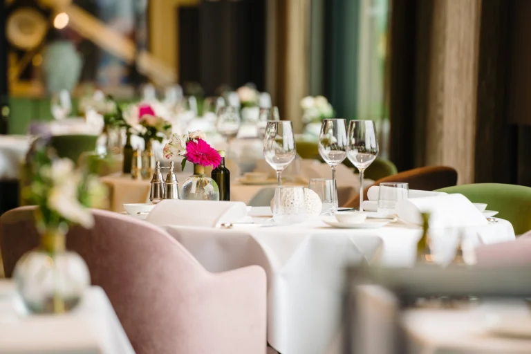 Laid tables with white cloths, wine glasses, pink flowers and blush velvet chairs in Marina's dining room