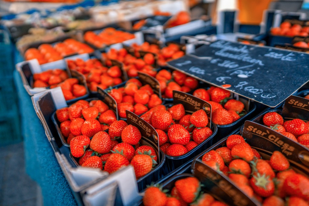 Market stall piled with punnets of fresh strawberries and tomatoes, with handwritten chalkboard price signs