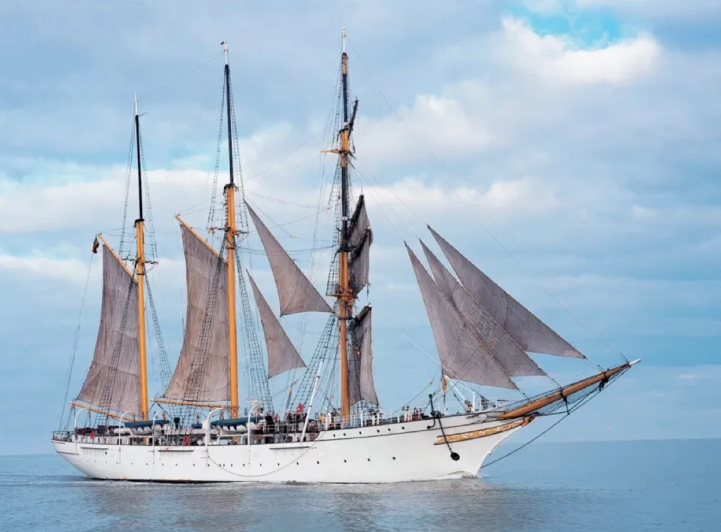 The white three-masted barquentine Mercator under full sail on a calm sea beneath a blue sky