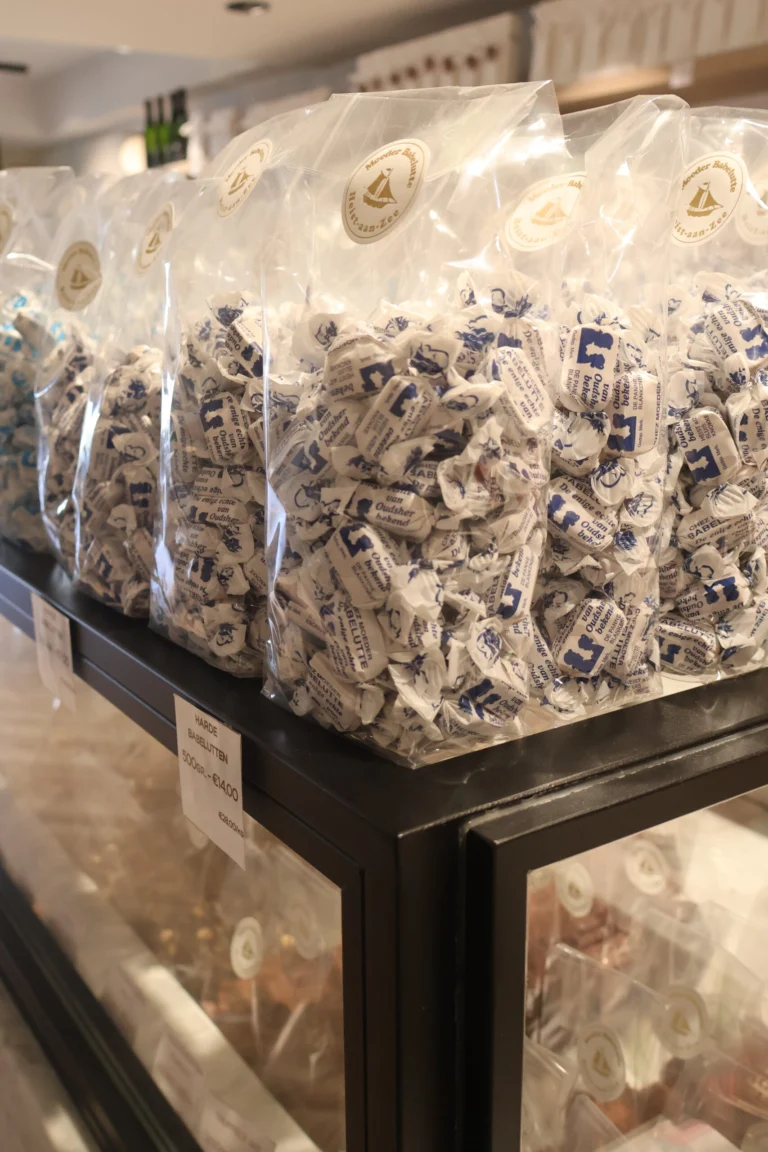 Large clear bags of individually wrapped babelutten in white and blue paper stacked on top of a glass chocolate counter