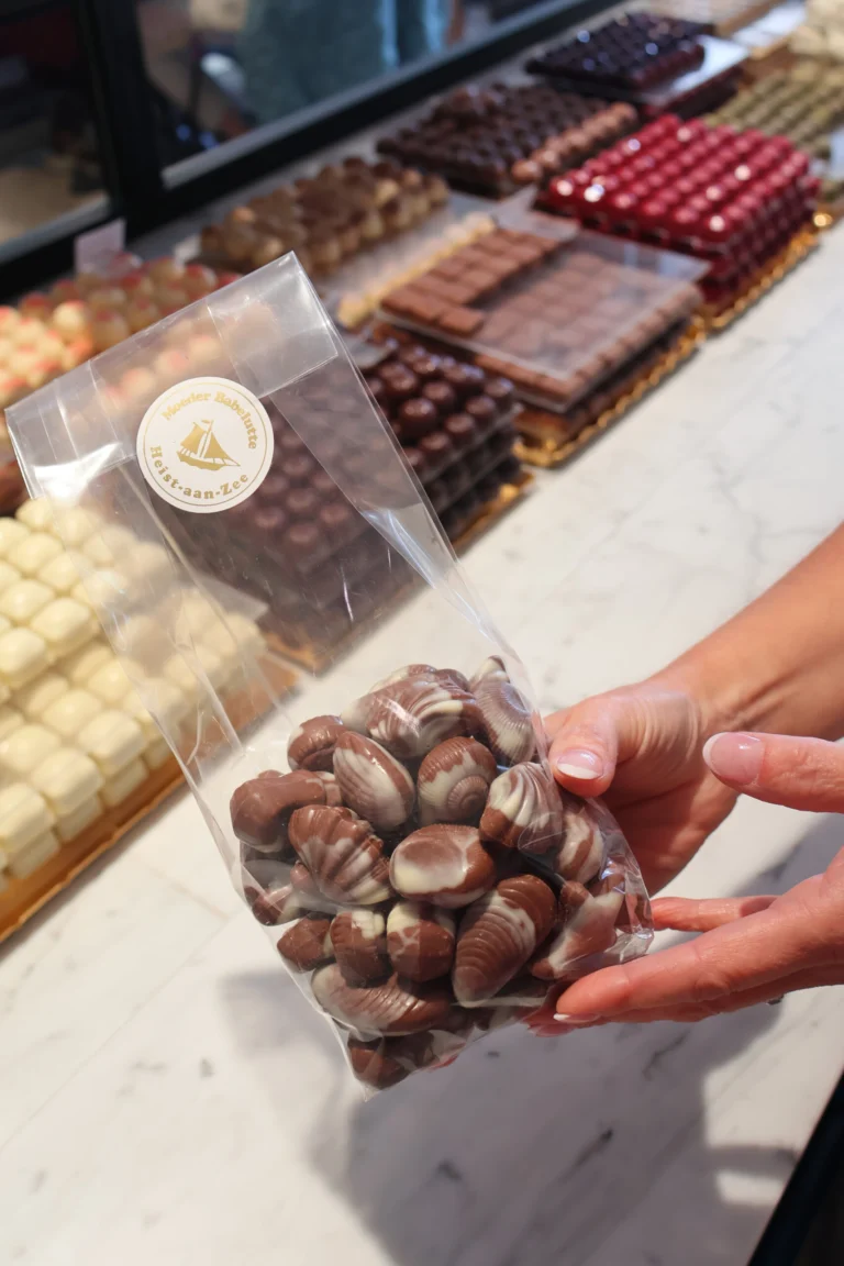 Hands holding a bag of marbled chocolate seashells in front of a marble counter lined with trays of pralines