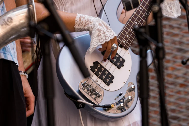 Close-up of a musician's hand on a pale blue bass guitar, with a lace cuff and microphone stand