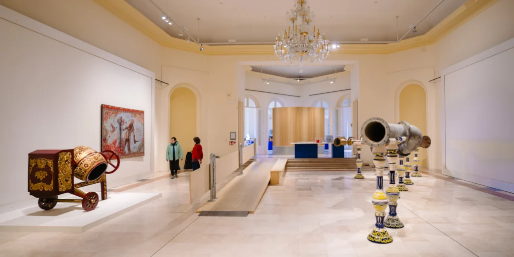 High-ceilinged exhibition hall in the Venetian Galleries with a chandelier, sculptures and a painting on white walls