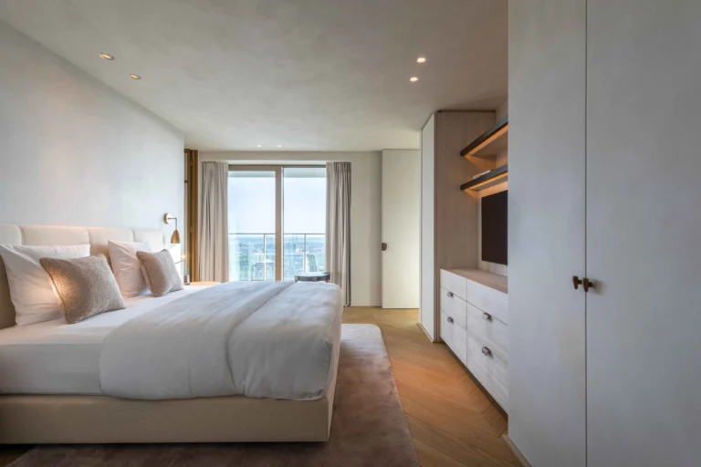 Calm bedroom in neutral tones with a large bed, built-in wardrobe and balcony door