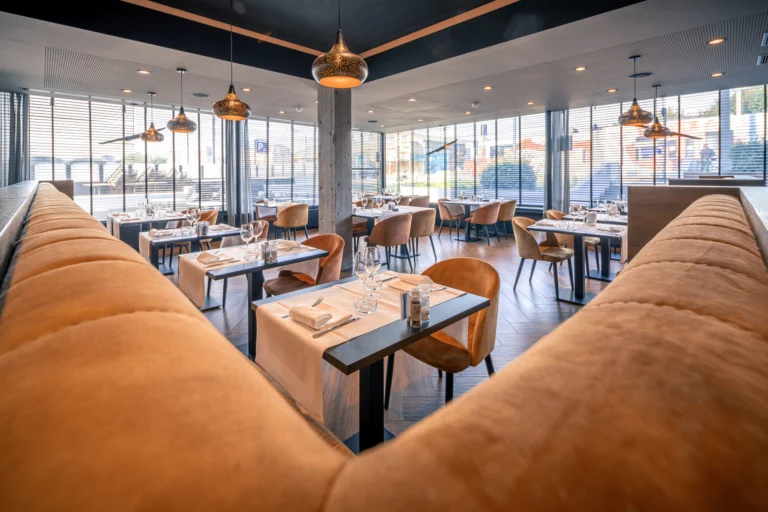 Hotel restaurant with tan leather banquettes, laid tables and copper pendant lamps by large street-facing windows