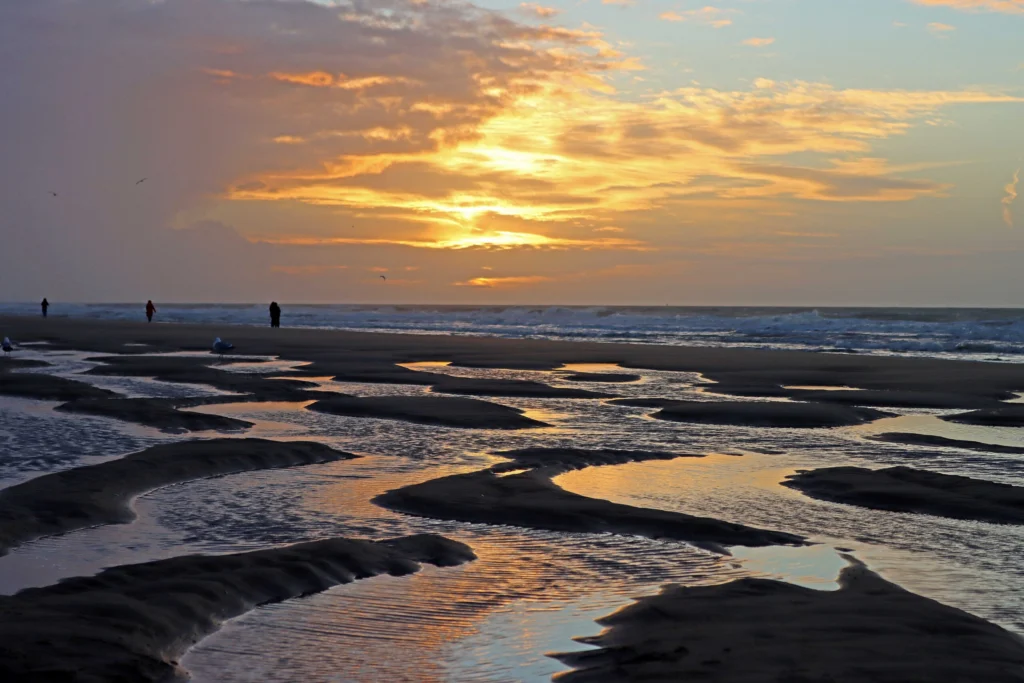 Ostend beach at low tide at sunset, with pools of seawater reflecting a golden sky and a few people walking at the water's edge
