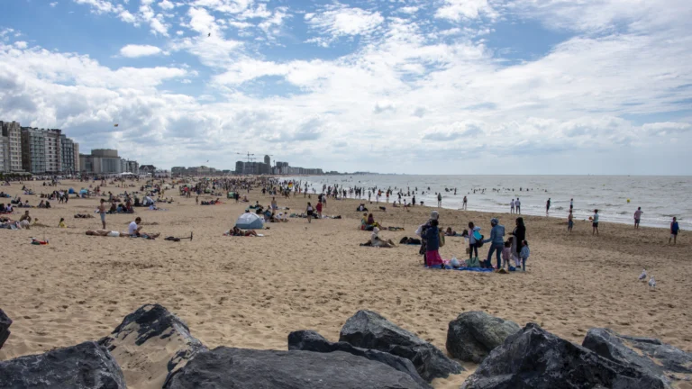 Busy sandy beach on a summer day, with seafront apartment blocks stretching along the coast