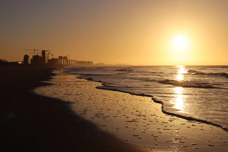 Golden sunset over the sea, reflected on the wet sand, with the seafront skyline in silhouette