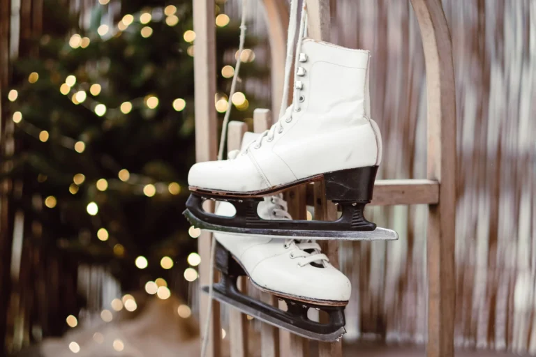 White ice skates hanging on a wooden sled in front of a Christmas tree with warm fairy lights