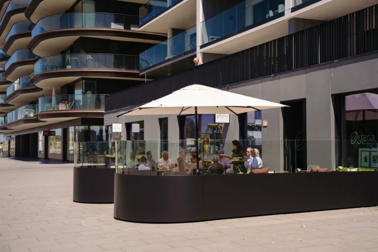 Guests seated on the glass-screened terrace of Osteria Marina under a white parasol, below a curved-balcony apartment building