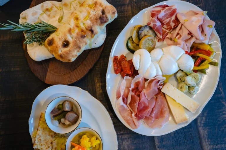 A platter of cured meats, burrata, cheese and grilled vegetables beside focaccia with rosemary and small dishes of pickles