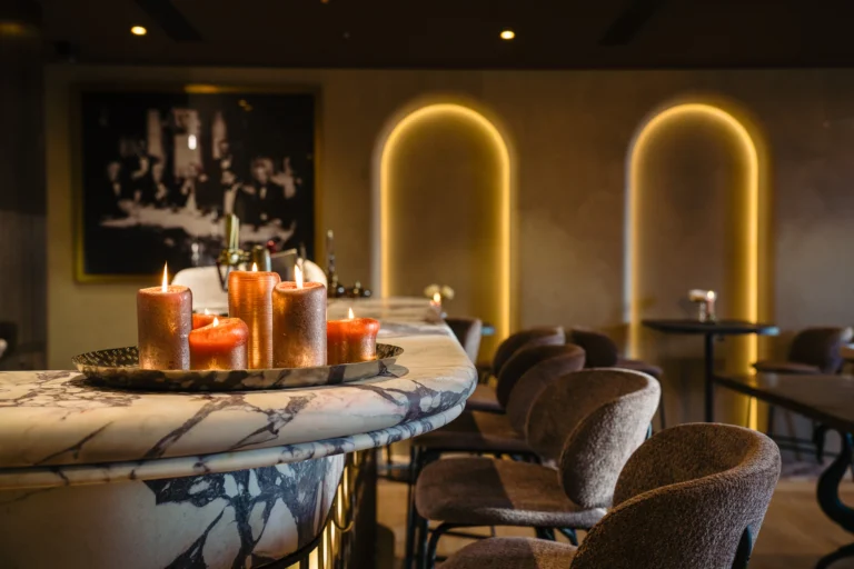 A curved marble-topped bar with lit candles and brown bar stools, in front of softly lit arched niches on the wall of Osteria Marina