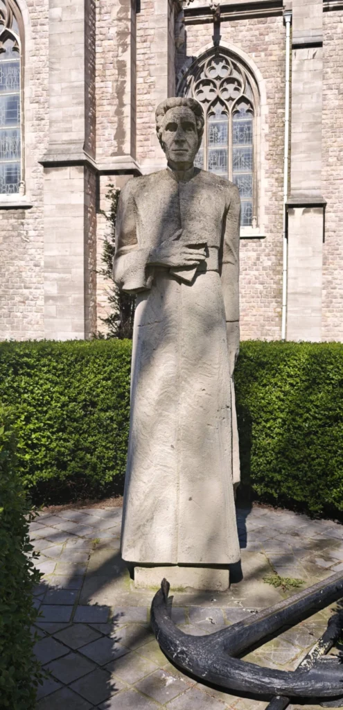 Stone statue of Paster Pype in a long cassock beside St Peter and St Paul's Church, with an anchor