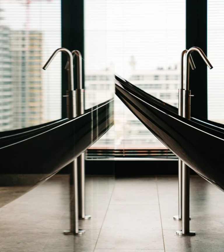 Two black hanging baths with tall chrome taps in front of floor-to-ceiling windows overlooking apartment towers