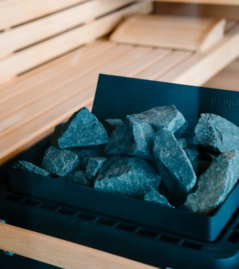 Close-up of grey-blue sauna stones in the heater below pale wooden sauna benches