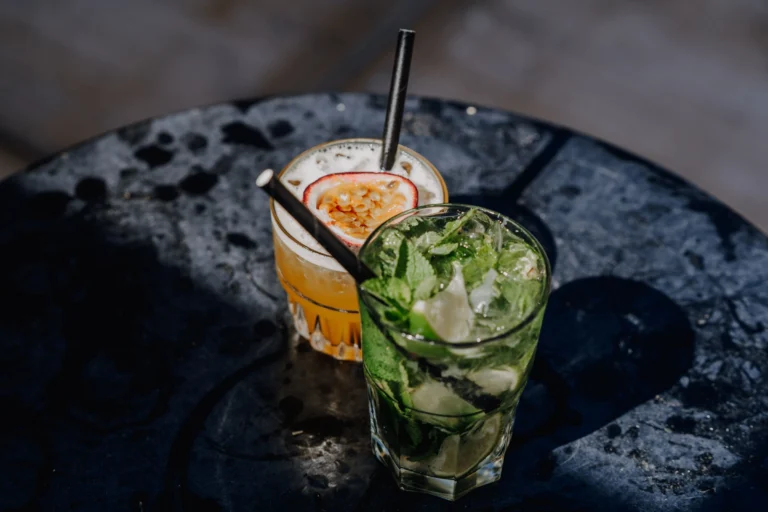 A passion fruit cocktail and a mojito with straws on a dark table