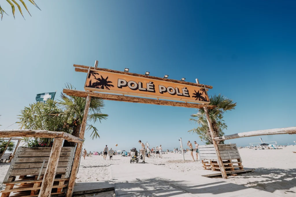Wooden Polé Polé arch with palm trees on the sand, with the beach and sea behind under a blue sky